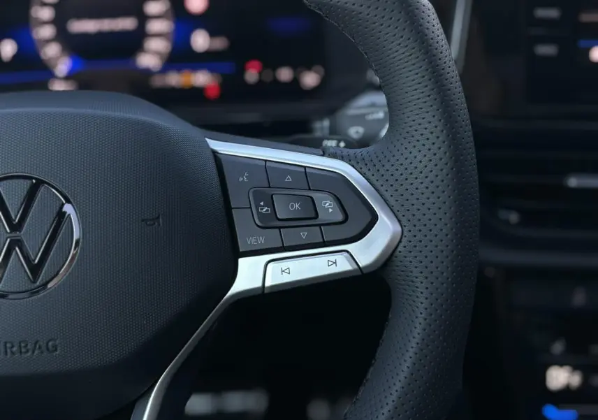 Gros plan sur le volant en cuir perforé du Volkswagen T-Roc 2025, avec commandes multifonctions et logo VW visible.