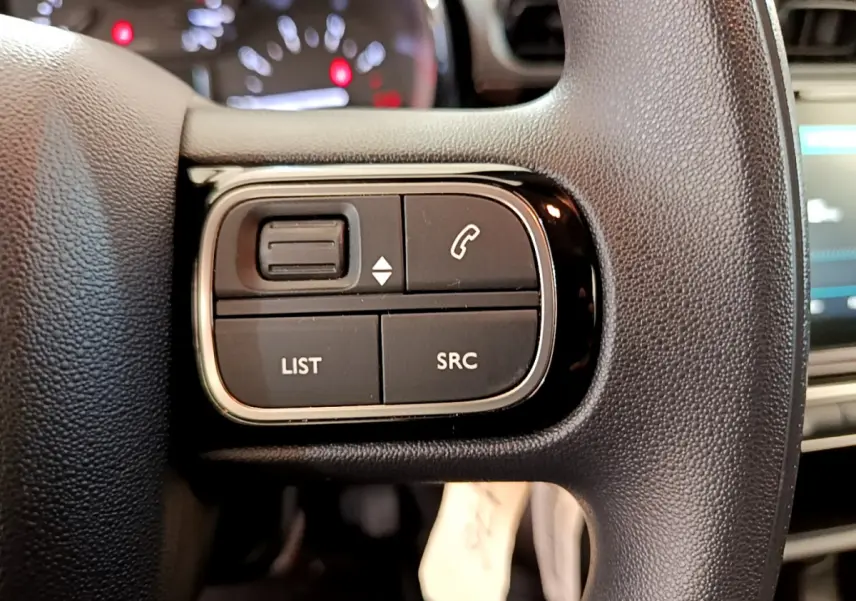 Gros plan sur les commandes gauche du volant noir d'une Citroën C3 PureTech 82 essence 2019, avec tableau de bord flou en arrière-plan.