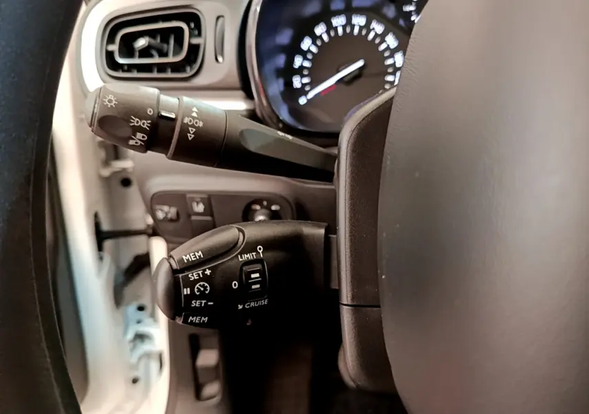 Gros plan sur les commandes de régulateur et feux au volant d'une Citroën C3 blanche, tableau de bord en arrière-plan.