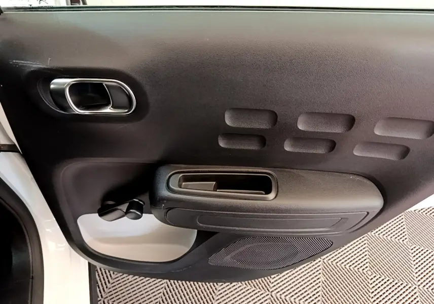 Intérieur côté gauche de la porte avant d'une Citroën C3 blanche 2019, avec poignée et commande de vitre manuelle.