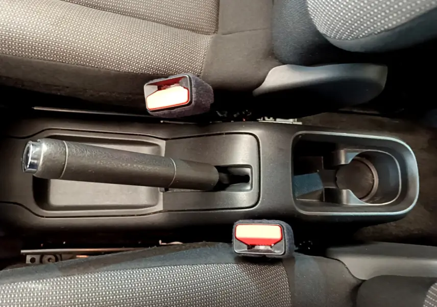 Vue plongeante sur la console centrale noire de la Citroën C3 PureTech 82, avec frein à main et ceintures rouges.