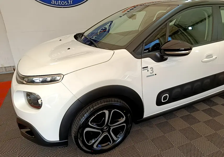 Vue 3/4 avant gauche d'une Citroën C3 blanche avec protections latérales noires et jantes stylisées noires.