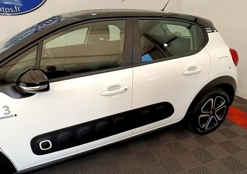 Profil côté gauche d'une Citroën C3 blanche avec toit noir et protections latérales noires distinctives.