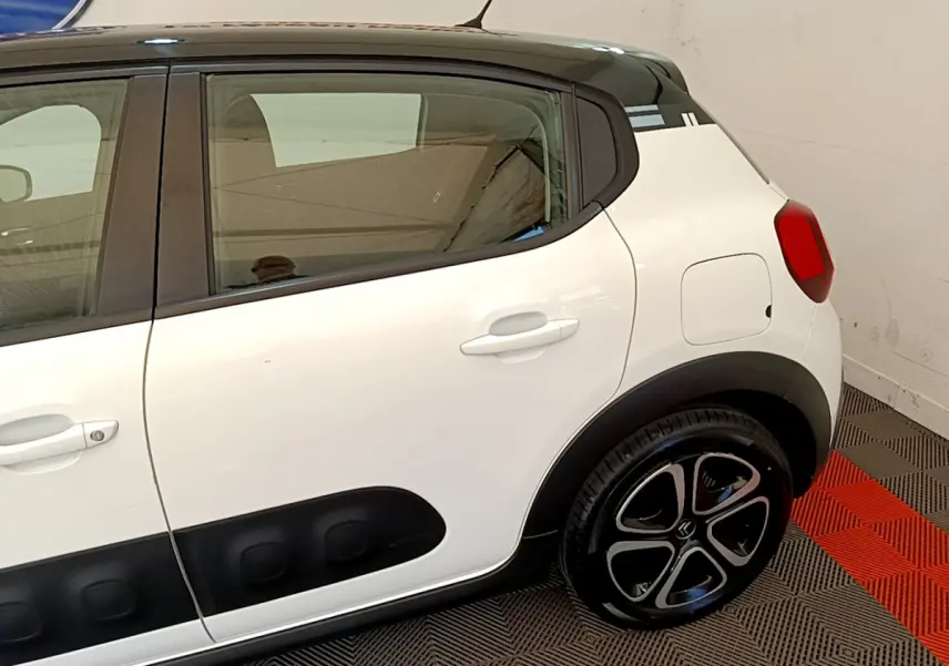 Vue latérale côté droit d'une Citroën C3 blanche avec protections noires et jantes stylisées en intérieur showroom.