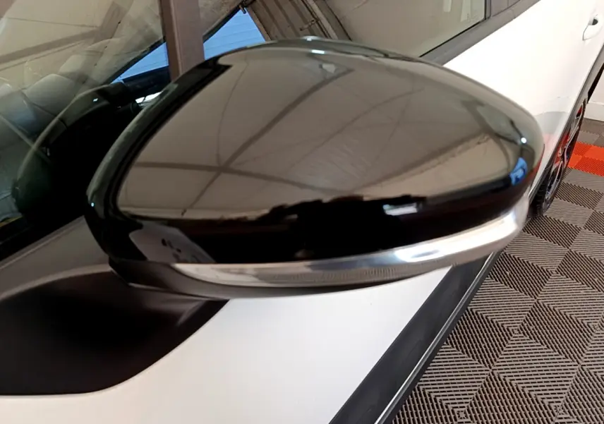 Rétroviseur noir brillant côté conducteur d'une Citroën C3 blanche vue en gros plan depuis l'avant gauche.