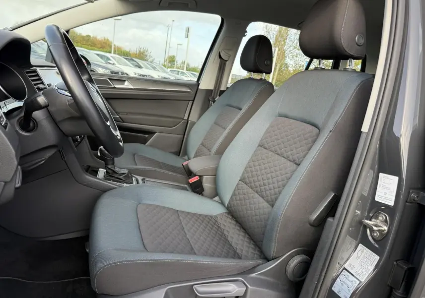 Vue intérieure côté conducteur de la Volkswagen Golf Sportsvan gris Urano, montrant les sièges avant en tissu bicolore.