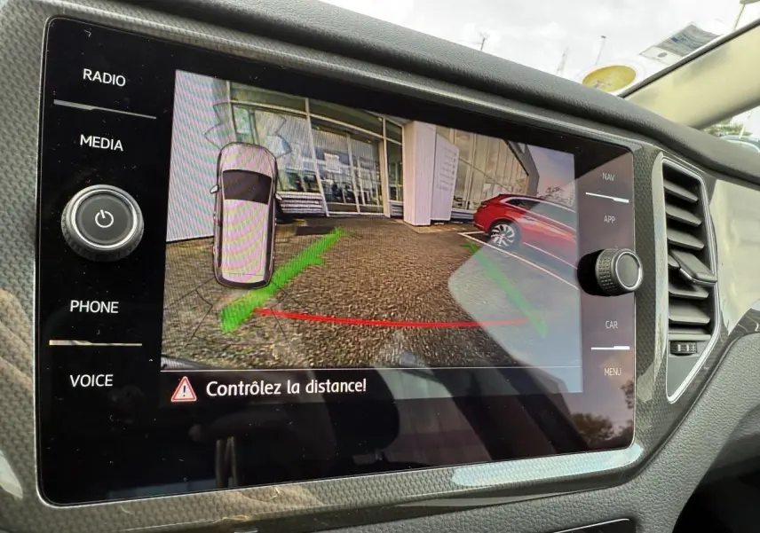 Écran de la caméra de recul dans une Volkswagen Golf Sportsvan gris Urano, affichant la zone arrière avec guidage de distance.