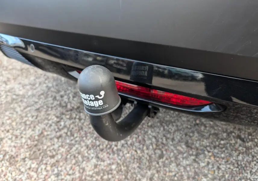 Gros plan sur l'attelage col de cygne noir à l'arrière d'une Citroën C4 rouge foncé, avec feu arrière intégré.