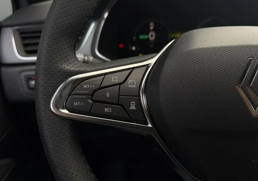 Gros plan sur le volant perforé côté gauche du Renault Captur gris, avec commandes de régulateur et logo central.