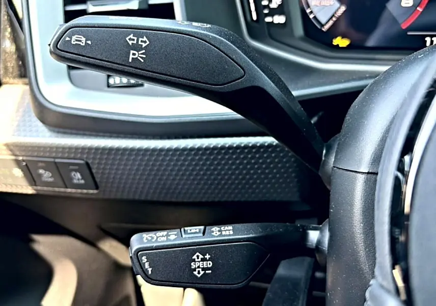 Gros plan sur les commandes au volant noir de l'Audi A1 Sportback 2026, avec tableau de bord numérique en arrière-plan.