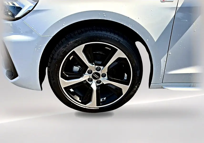 Gros plan sur la roue avant gauche d'une Audi A1 Sportback blanche avec jante alu et badge S line visible.