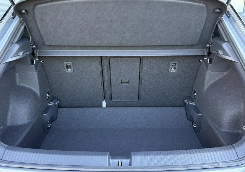 Coffre ouvert du Volkswagen T-Roc gris pyrite, vue arrière montrant l'espace de chargement et la trappe centrale.