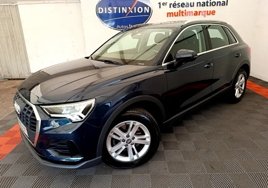 Audi Q3 bleu foncé vu en 3/4 avant droit dans un showroom avec jantes alliage et feux LED allumés.