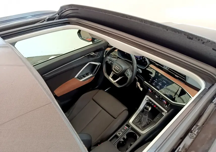 Vue intérieure côté conducteur de l'Audi Q3 35 TDI bleu, montrant le volant cuir et la console centrale moderne.