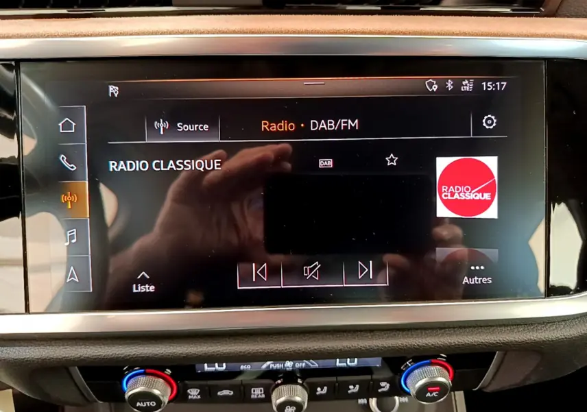 Écran tactile central affichant la radio DAB/FM sur Audi Q3 bleu, avec commandes climatisation en dessous.