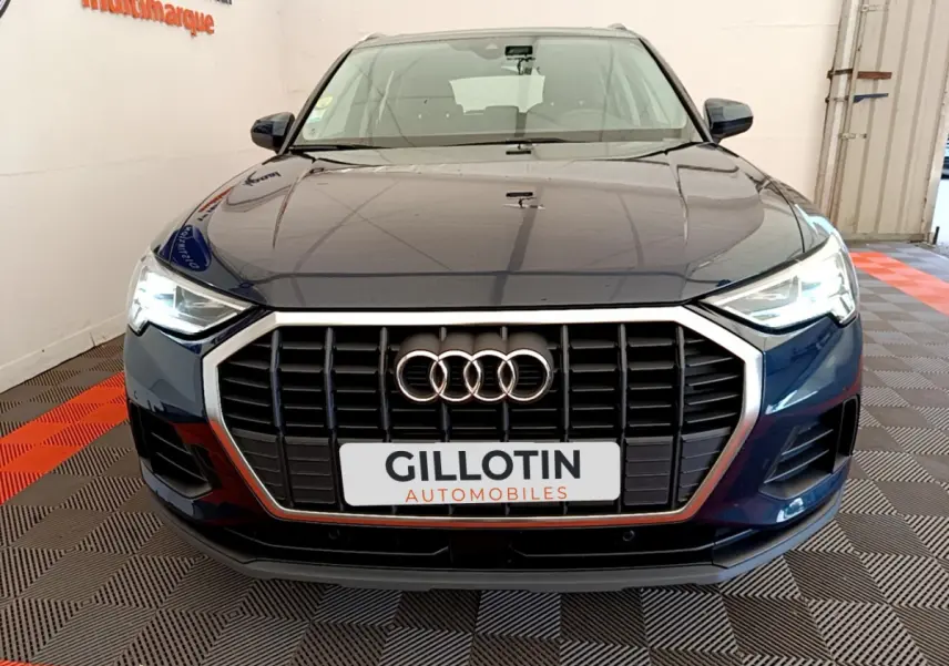 Vue frontale d'un Audi Q3 bleu 2020 avec calandre noire et phares LED allumés dans un showroom.