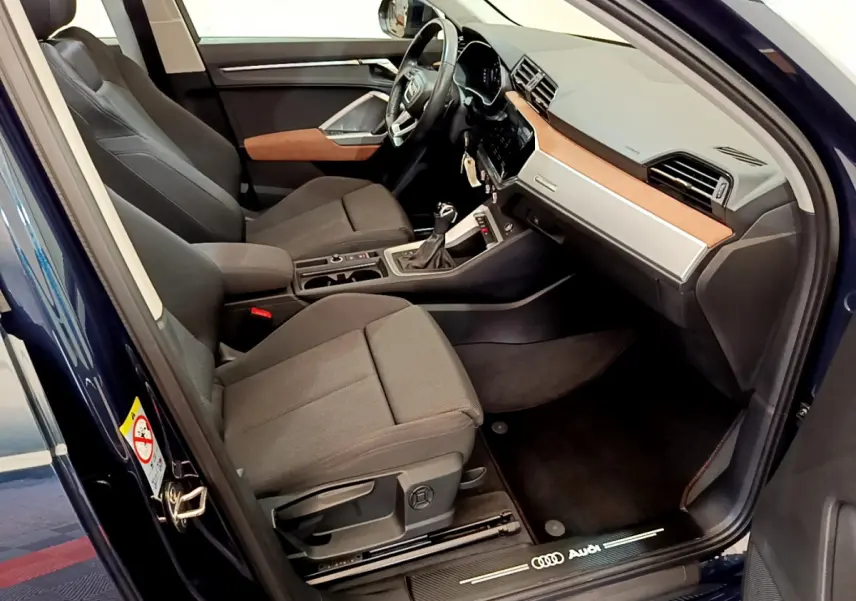 Intérieur avant droit de l'Audi Q3 bleu 2020, sièges gris, tableau de bord avec insert bois et volant cuir multifonctions.