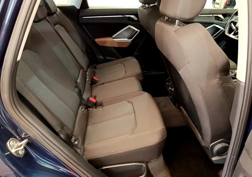 Vue intérieure côté arrière gauche de l'Audi Q3 bleu 35 TDI, montrant la banquette arrière en tissu gris foncé.