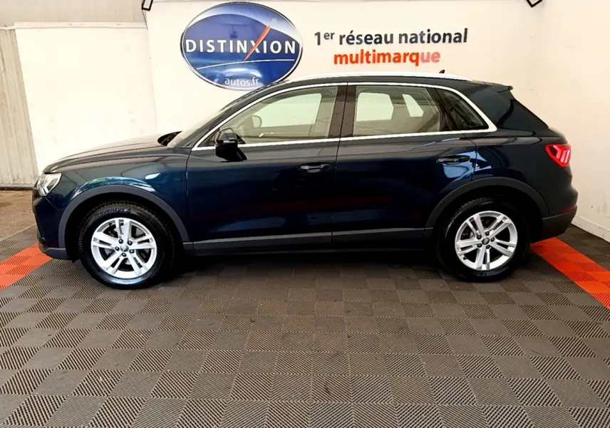 Audi Q3 bleu 2020 vue de profil côté gauche, avec jantes alliage et feux arrière LED visibles en intérieur showroom.