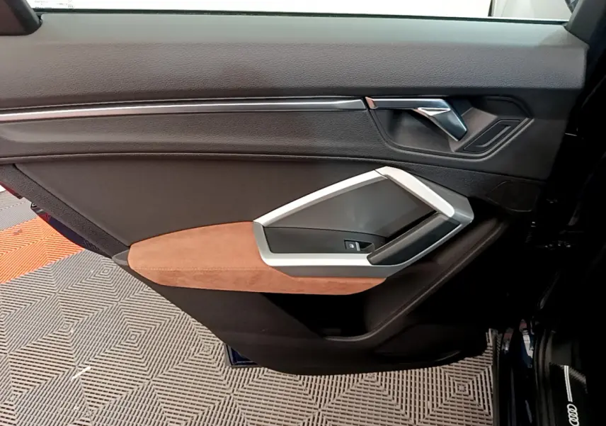 Gros plan sur la porte avant gauche de l'Audi Q3 bleu 2020, avec garniture noire et accoudoir marron clair en alcantara.