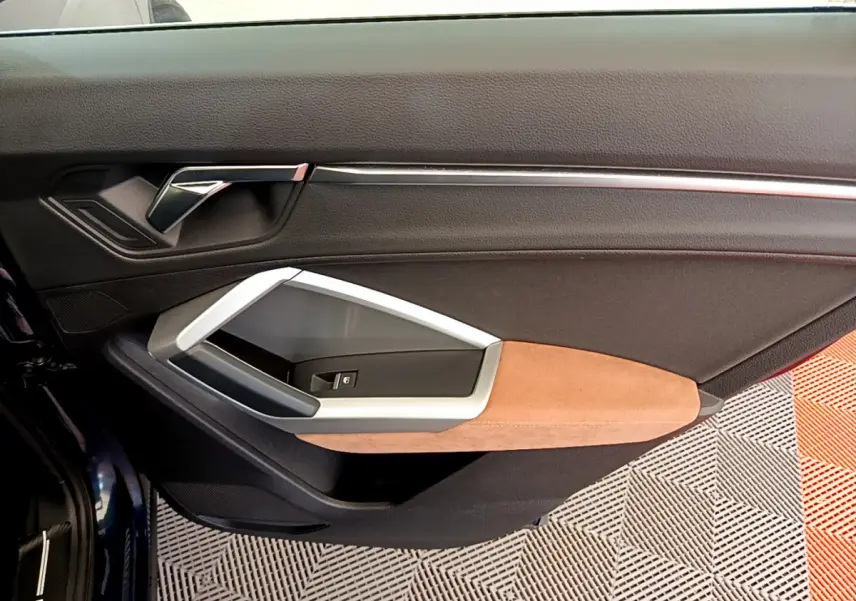Gros plan sur la garniture intérieure côté gauche de la porte d'un Audi Q3 bleu avec accoudoir beige et insert argenté.