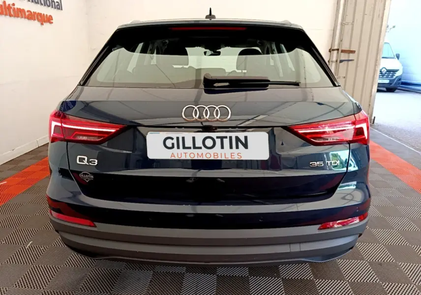 Vue arrière d'un Audi Q3 bleu 35 TDI avec feux LED et logo distinctif sur un sol damier intérieur.