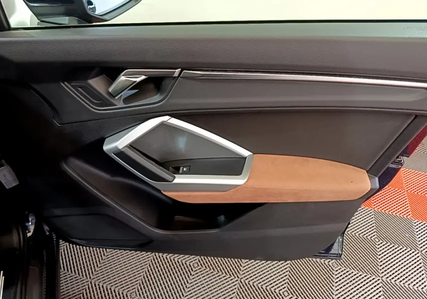 Gros plan sur la porte côté gauche de l'Audi Q3 bleu, avec garniture marron et poignée argentée moderne.