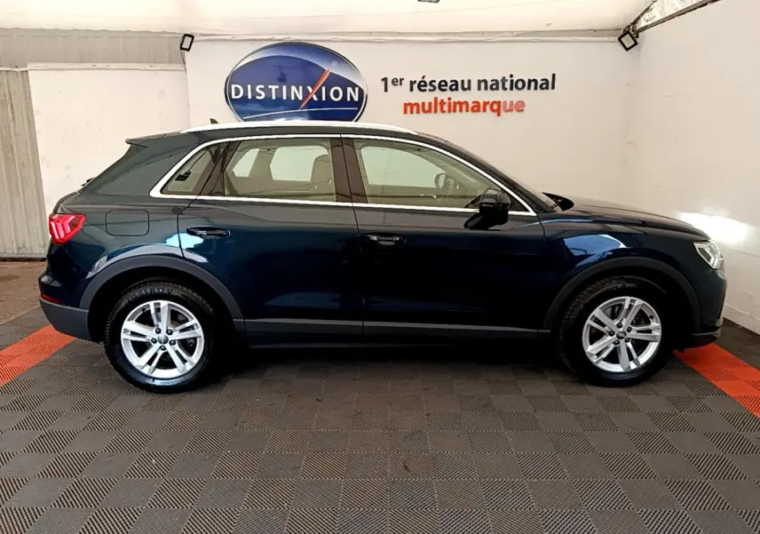 Audi Q3 bleu foncé vu de profil côté gauche, avec jantes alliage et feux arrière LED visibles en intérieur showroom.