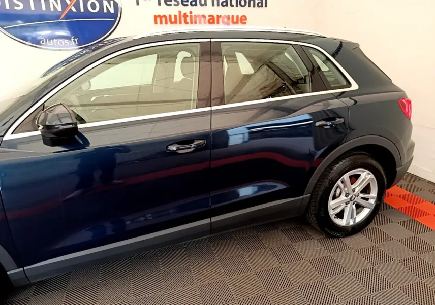 Profil côté gauche d'un Audi Q3 bleu 2020 avec jantes alliage et rétroviseurs noirs en intérieur showroom.