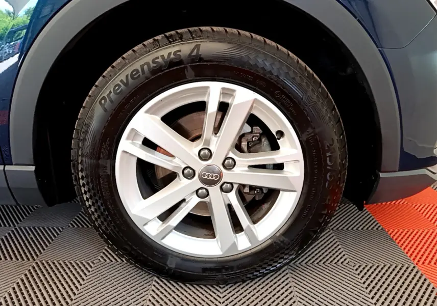 Gros plan sur la roue avant gauche d'un Audi Q3 bleu 35 TDI 150 S tronic avec jante argentée à 5 branches.