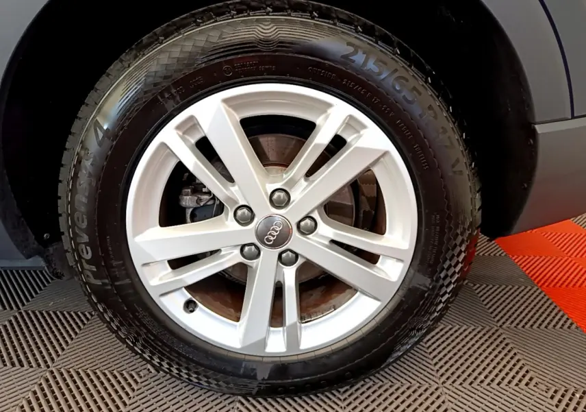 Gros plan sur la roue avant droite d'un Audi Q3 bleu 2020, mettant en valeur la jante argentée à cinq branches.