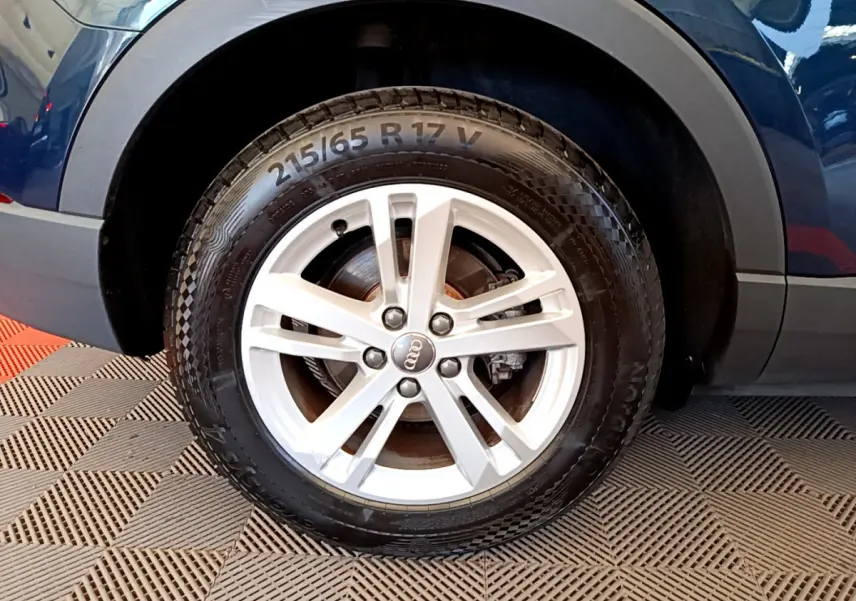 Gros plan sur la roue avant gauche d’un Audi Q3 bleu 2020 avec jante alliage argentée et pneu 215/65 R17.