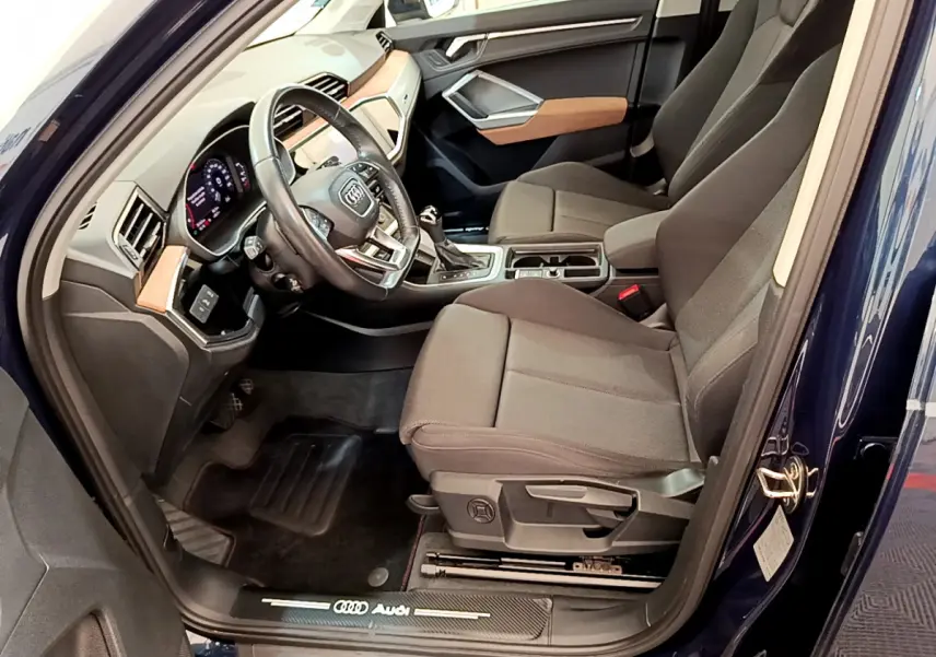 Intérieur côté conducteur d’un Audi Q3 bleu 2020, avec sièges tissu gris et tableau de bord moderne.