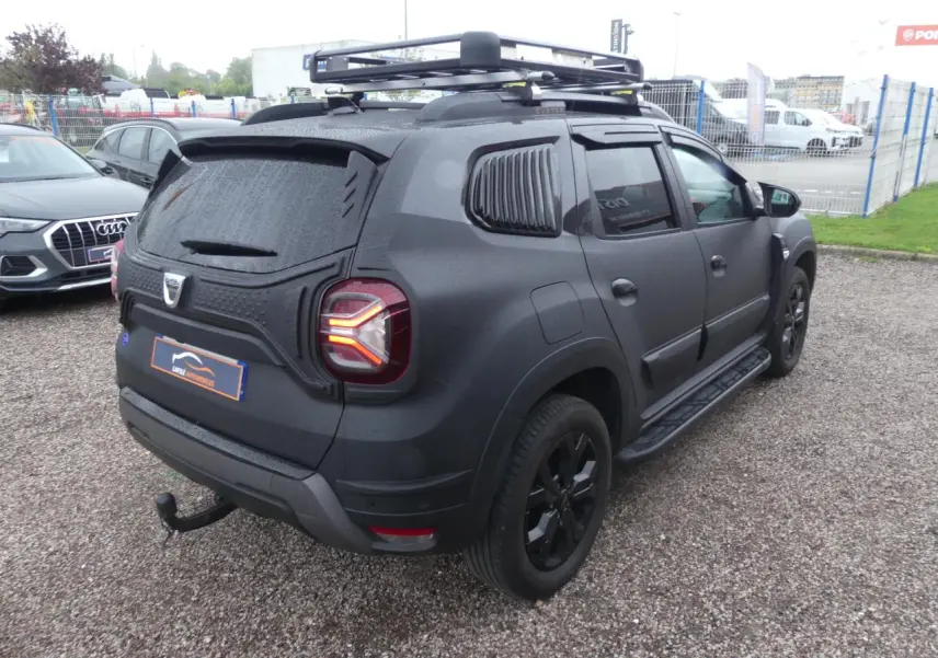 Vue 3/4 arrière droite du Dacia Duster noir 2023 avec galerie de toit, attelage fixe et marchepieds.