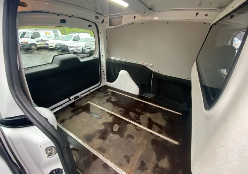 Vue intérieure du coffre arrière du Citroën Berlingo blanc, montrant l’espace de chargement vide avec sol en bois usé.