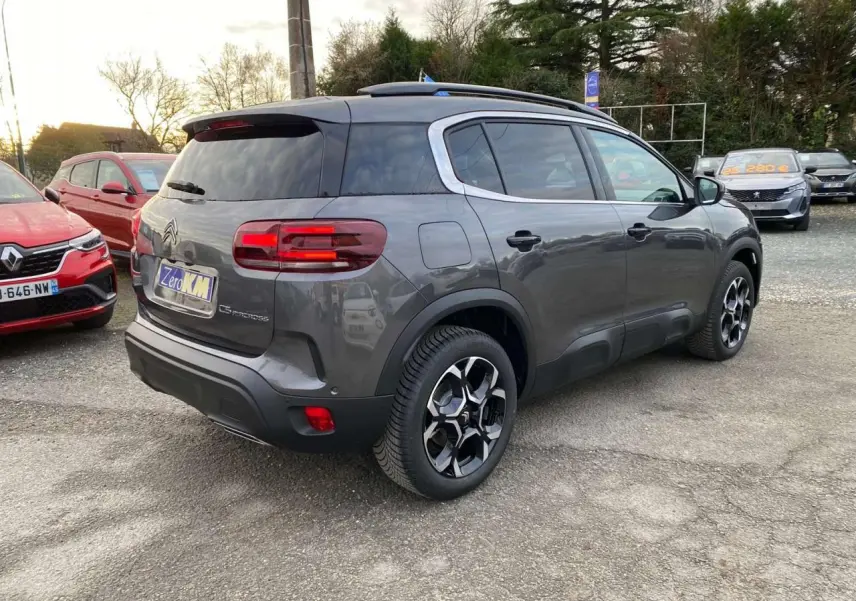 Vue 3/4 arrière droite d'un Citroën C5 Aircross gris platinium avec jantes alliage 18'' bi-ton sur parking.