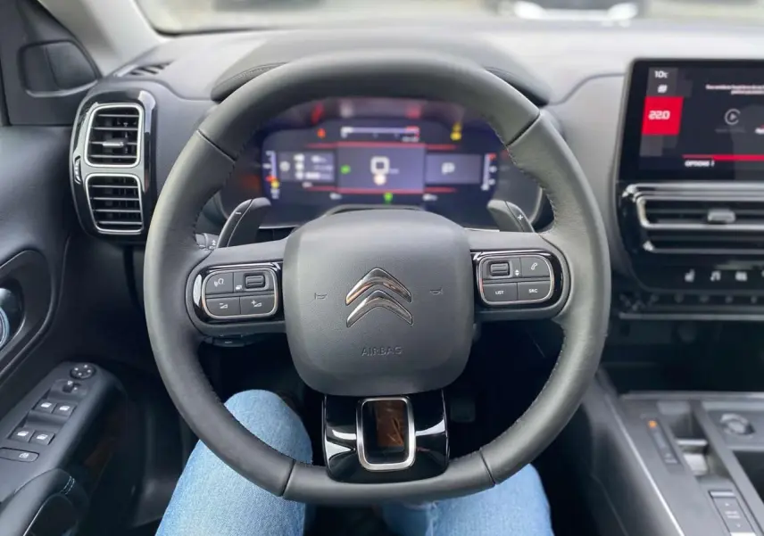 Vue intérieure centrée sur le volant noir du Citroën C5 Aircross 2025 avec tableau de bord numérique et écran tactile.