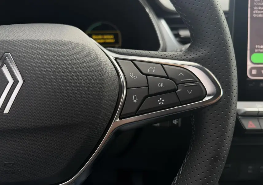 Gros plan sur le volant noir perforé du Renault Captur 2026 avec commandes multifonctions et logo central chromé.