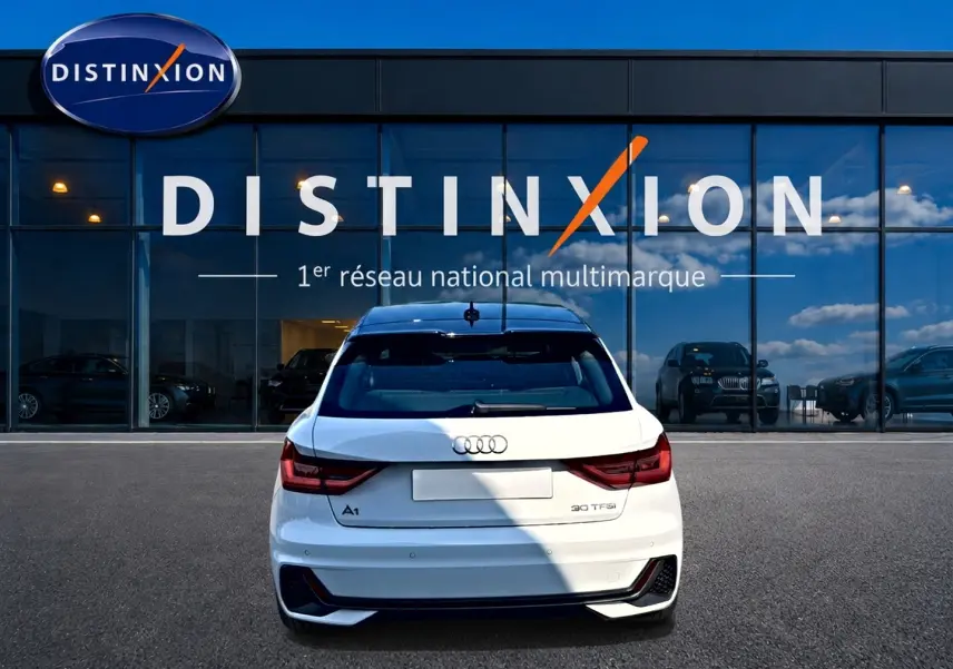 Vue arrière d'une Audi A1 Sportback blanche avec toit noir, feux LED et logo distinctif sur fond de vitrine Distinxion.