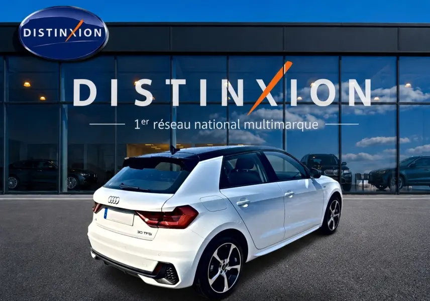 Audi A1 Sportback blanc toit noir en 3/4 arrière droit, avec jantes alu et becquet arrière visible devant showroom Distinxion.