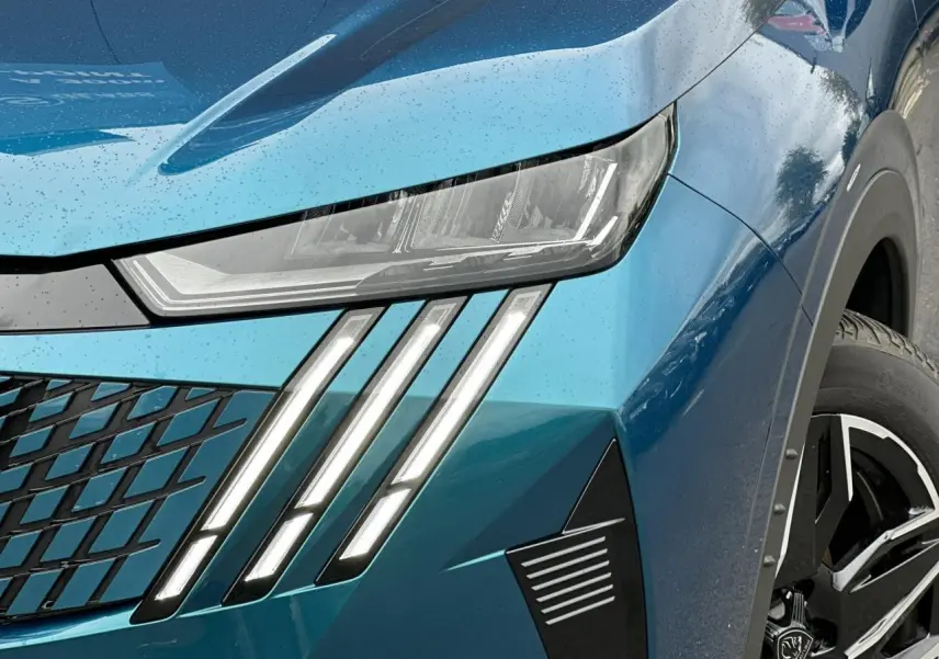Gros plan sur le phare avant gauche et la calandre du Peugeot 3008 Hybrid bleu Obsession avec jante alliage 19 pouces.