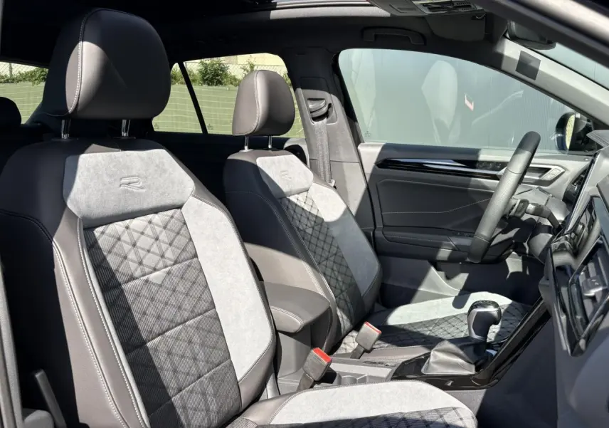 Intérieur avant du Volkswagen T-Roc 2025 avec sièges R-Line gris et noir, volant cuir et toit ouvrant visible.
