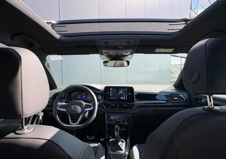 Intérieur noir du Volkswagen T-Roc 2025 vu de l'arrière, avec toit ouvrant en verre et tableau de bord digital.