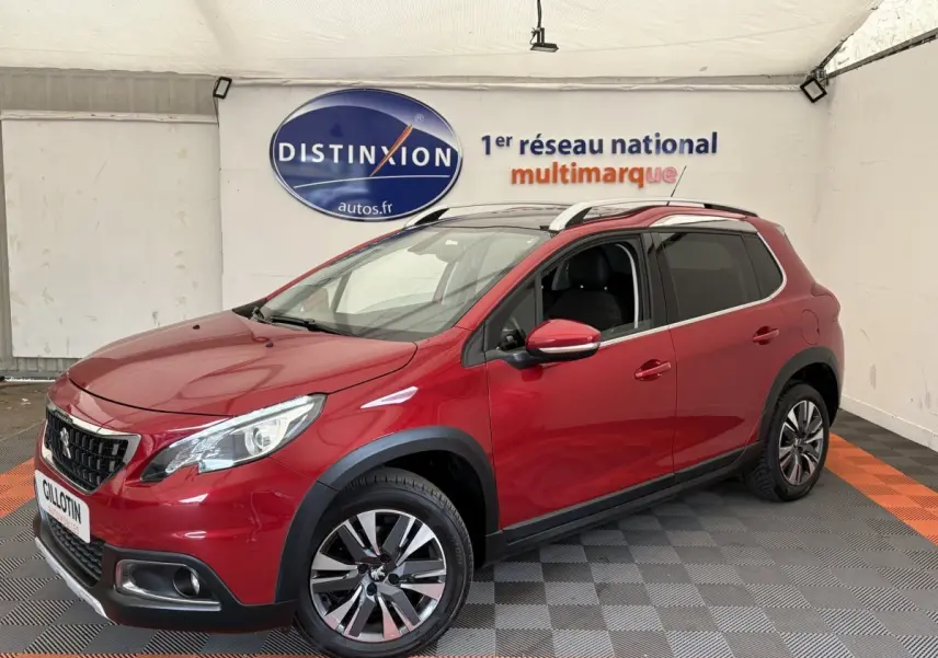Peugeot 2008 rouge vue 3/4 avant droit, avec jantes alliage et barres de toit chromées visibles.