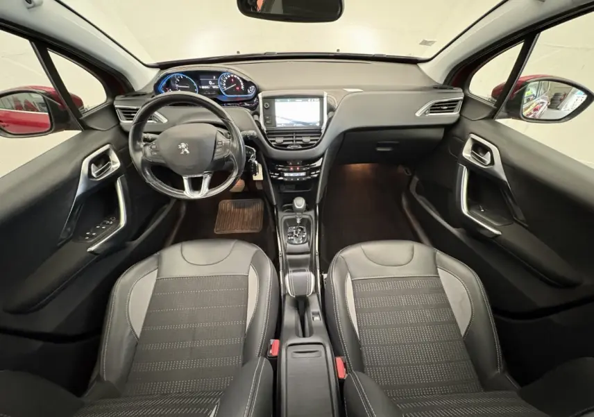 Vue intérieure avant de la Peugeot 2008 rouge, montrant le tableau de bord, volant cuir et sièges noirs.