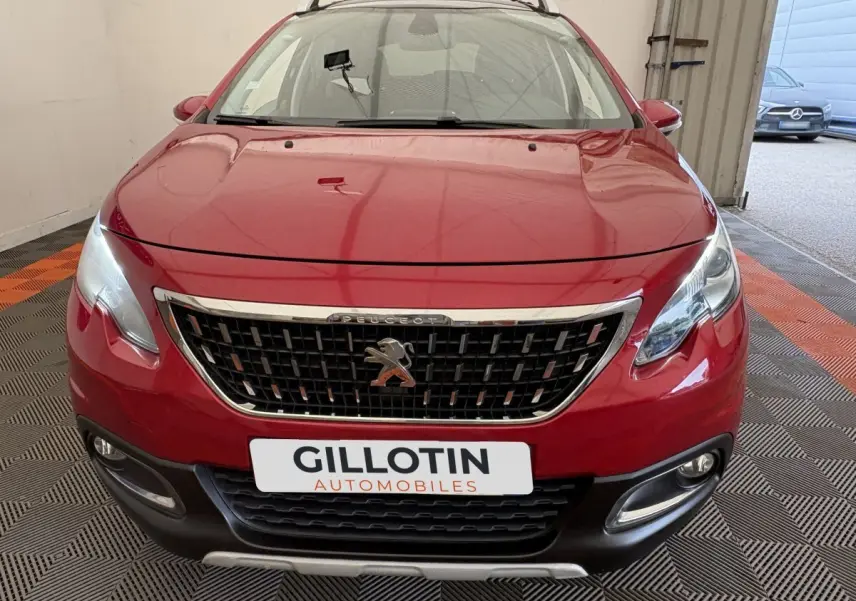 Vue frontale d'un Peugeot 2008 rouge avec calandre chromée et phares allumés dans un garage.
