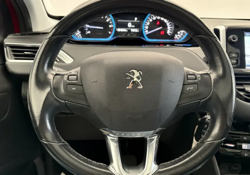Vue rapprochée du volant cuir noir de la Peugeot 2008 rouge avec tableau de bord digital et commandes intégrées.