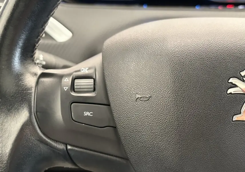 Gros plan sur le volant cuir noir du Peugeot 2008 avec commandes audio intégrées et logo lion central.