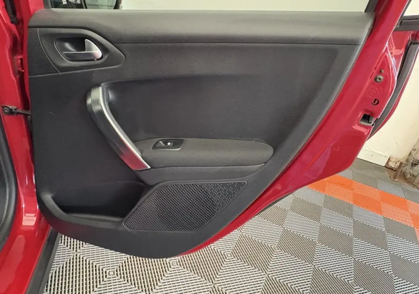 Porte arrière gauche ouverte d'une Peugeot 2008 rouge, montrant le panneau intérieur noir avec poignée chromée.