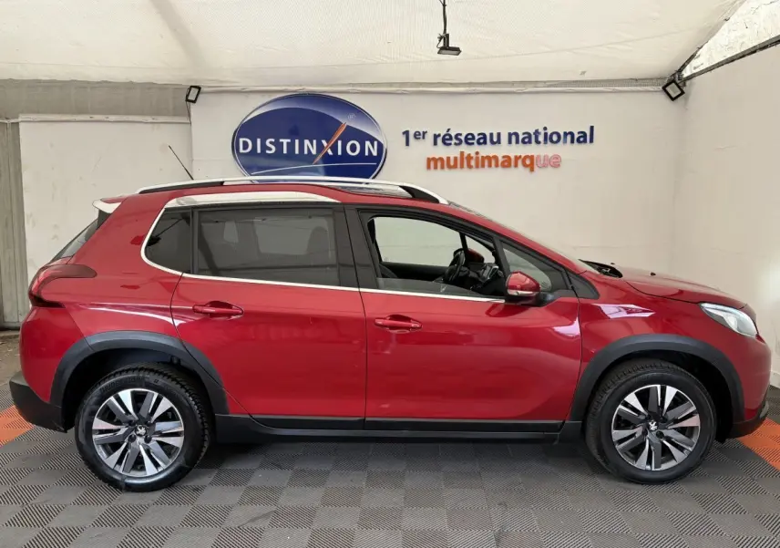 Profil droit d'un Peugeot 2008 rouge 2019 avec jantes alliage et barres de toit chromées en showroom.